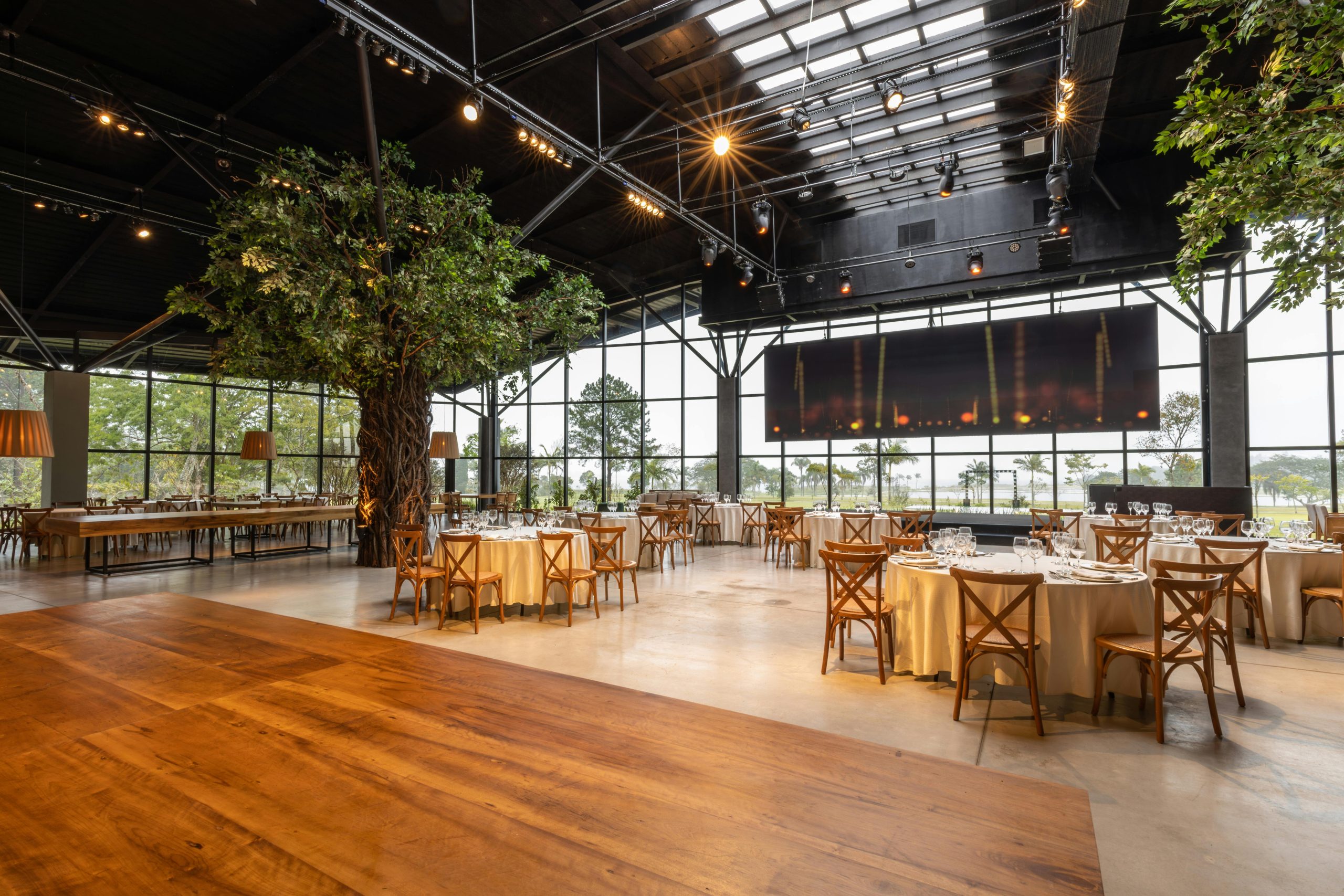 Spacious and elegant banquet hall with indoor trees, modern decor, and large windows for events or gatherings.